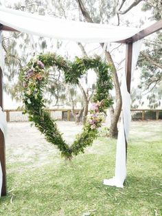 a heart - shaped wreath is tied to the side of a wooden structure with white drapes