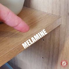 someone pointing to the word melamine on a wooden shelf