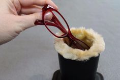 someone is holding their glasses over the top of a small cup with fur lining it