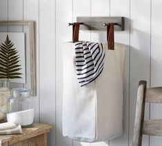 a white bag hanging on the wall next to a wooden chair and potted plant