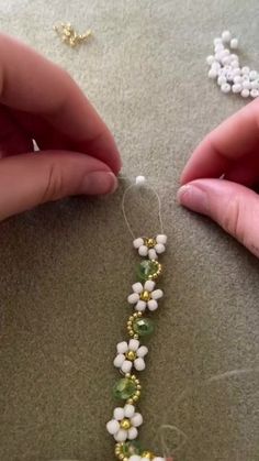 two hands are working on a beaded necklace with white flowers and green beads in the middle