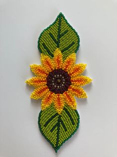 a beaded brooch with a sunflower on it's back end and green leaves