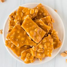 a white plate topped with pieces of peanut butter fudge next to peanuts on a table