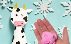 a hand holding a pink toy next to a cow and snowflakes on a blue background