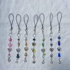 six different colored charms hanging from silver hooks on a white cloth covered tablecloth in various shapes and sizes