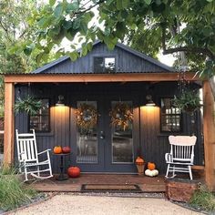 two white rocking chairs sitting on top of a wooden porch next to a black shed