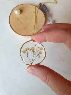 a hand holding a glass pendant with dried flowers on it, next to a piece of wood