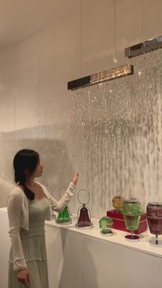 a woman standing in front of a display of glass vases and lamps with water droplets hanging from the ceiling