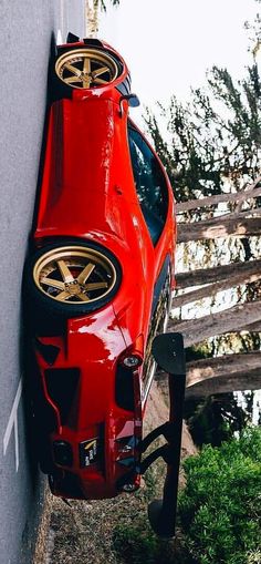 a red sports car parked next to a white wall with gold rims on it