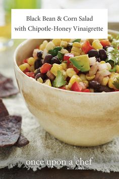 a wooden bowl filled with black beans, corn and avocado next to tortilla chips