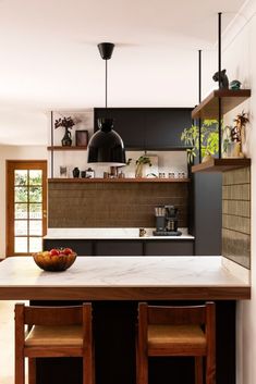 a bowl of fruit sitting on top of a kitchen counter next to two stools