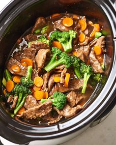 a crock pot filled with beef, broccoli and carrots