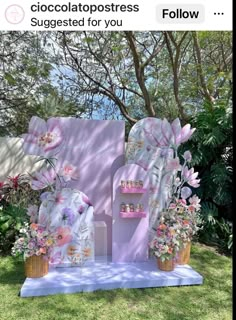 a pink and white sign with flowers on it in front of some trees, grass and bushes