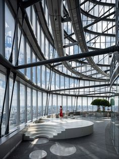 a woman in a red dress is walking through a large room with glass walls and floor to ceiling windows