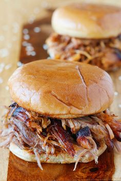 two pulled pork sandwiches sitting on top of a wooden cutting board