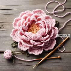 a crocheted pink flower sitting on top of a wooden table next to knitting needles