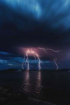 lightning striking over the ocean with boats in the water