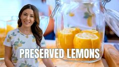 a woman standing in front of a glass pitcher filled with lemons on top of a table