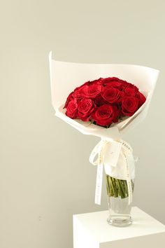 a bouquet of red roses in a clear vase on a white pedestal against a wall