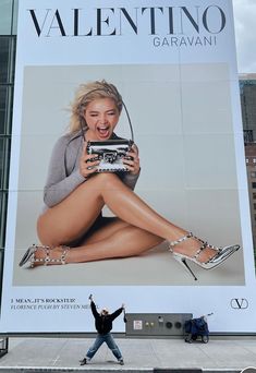 a woman standing in front of a giant advertisement for a women's shoe brand