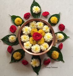 a bowl filled with flowers and leaves on top of a white table next to green leaves