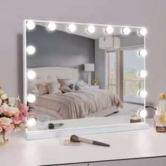 a vanity mirror with lights on it next to a bouquet of flowers and makeup brushes