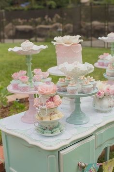 a table topped with cakes and cupcakes on top of cake stands in the grass