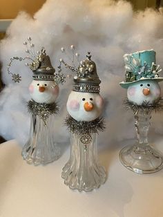 three snowmen with hats and silver decorations on top of a white cloth covered table