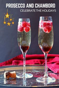 two champagne flutes with raspberries in them on a tray