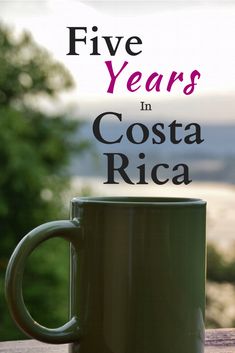 a green coffee mug sitting on top of a wooden table next to a window with the words five years in costa rica