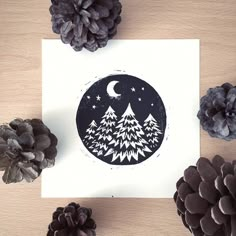 pine cones are arranged around a card with a black and white illustration of trees on it