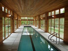 an indoor swimming pool surrounded by windows and wood paneled walls, with stairs leading up to it