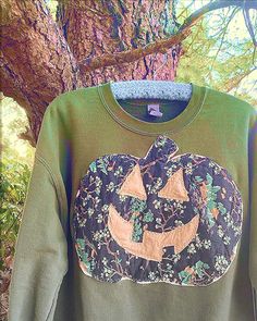 a green sweatshirt with a pumpkin on it is hanging in front of a large tree