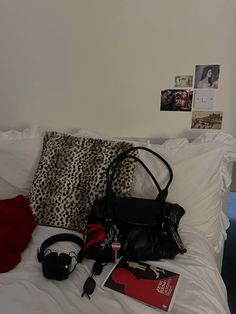 a black purse sitting on top of a white bed next to a red book and other items