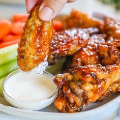 a person dipping sauce on chicken wings with carrots and celery in the background