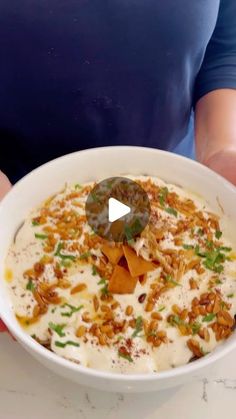 a person holding a bowl of food with nuts and ranch dressing in front of them