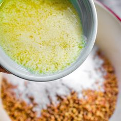 a person holding a cup filled with yellow liquid and granola in front of them