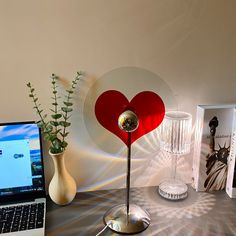 a laptop computer sitting on top of a desk next to a vase with a heart