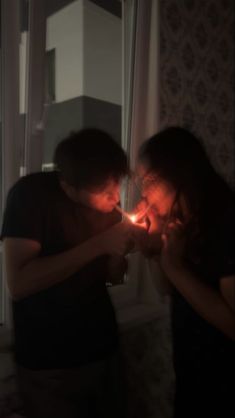 two people standing next to each other in front of a window with the lights on