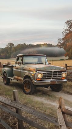 an old pick up truck is parked on the side of a road near a fence