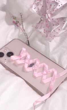 an iphone case with pink ribbons attached to it on a white sheeted bed next to a cell phone