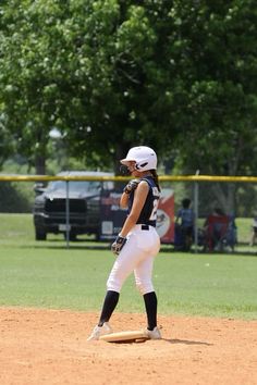 a girl in white and black baseball uniform standing on a field with her mitt up