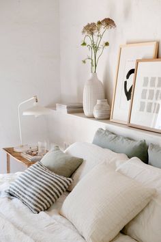 a bed with white sheets and pillows on top of it next to two framed pictures