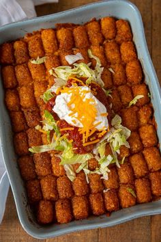 a blue dish filled with tater tots covered in cheese and lettuce