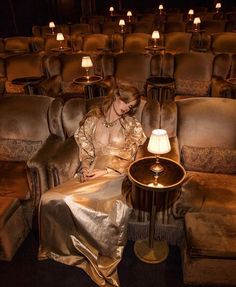 a woman sitting in a chair next to a table with a lamp on top of it