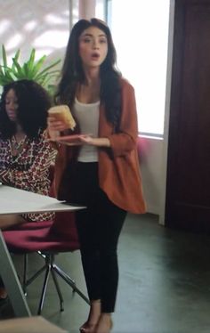 a woman standing in front of a table holding a piece of bread and looking at the camera