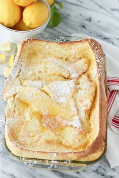 a loaf of bread with powdered sugar on top and two bowls of fruit in the background