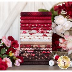 a stack of red and white quilts next to some pink flowers on a table