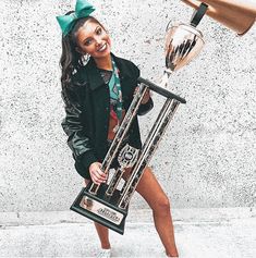 a young woman holding a trophy next to a giant metal object in front of a wall