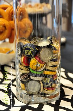 a glass vase filled with lots of different types of beer bottle caps and cookies on top of a black and white tablecloth